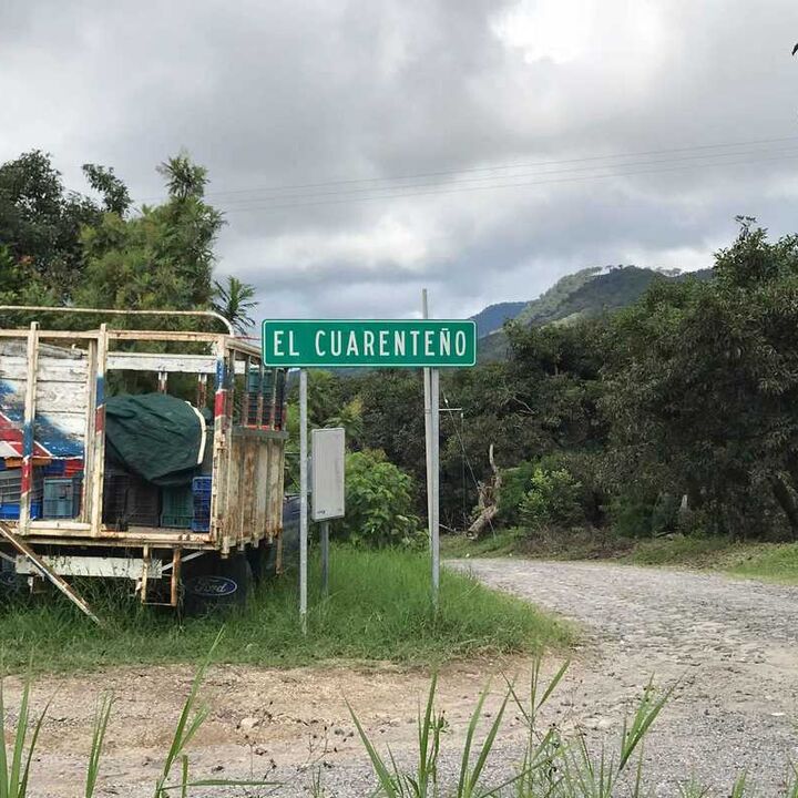 Sign for "El Guariento" next to a parked trailer and a dirt road in a rural area.
