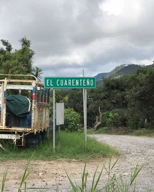 Sign for "El Guariento" next to a parked trailer and a dirt road in a rural area.