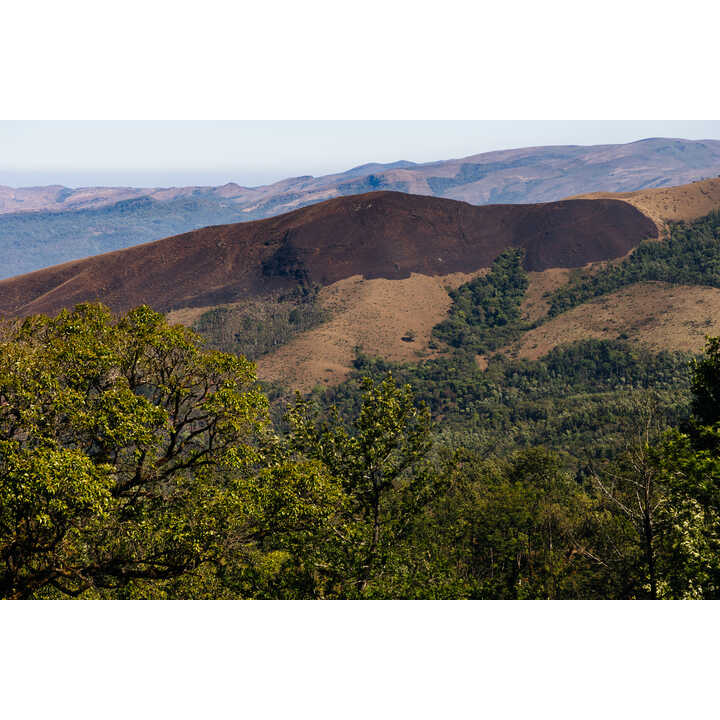 Mountain landscape with lush greenery and a brown volcanic slope in the background.