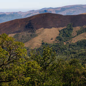 Mountain landscape with lush greenery and a brown volcanic slope in the background.
